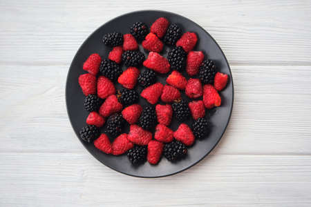 Fresh organic summer berries mix in round black table on dark wooden table background. Raspberries and blackberries. top viewの写真素材