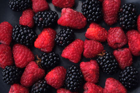 Background from fresh organic blackberries and raspberries, close up. Lot of ripe juicy wild fruit raw berries in a black plate. Top view blackberry and raspberry. Macro, selective focusの写真素材