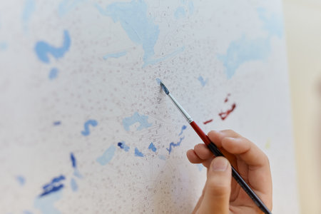 Close up painting by numbers. Kid's hand drawing with paintbrush on numbered canvas. Creative hobby...