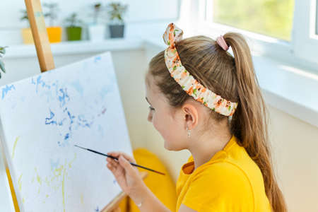 Adorable cute little girl child draws on the easel. Painting training at home. children's...
