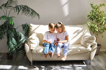 family, children, technology and home concept - smiling brother and sister with tablet pc computer...