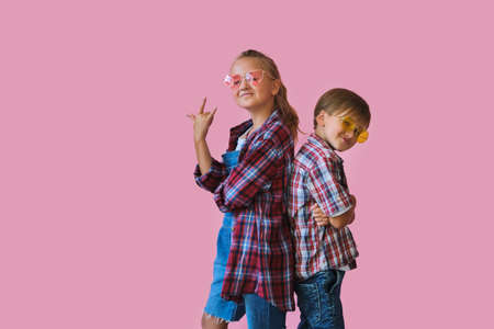 Cute stylish little girl and boy in color sunglasses dressed in plaid shirts looking at camera and...