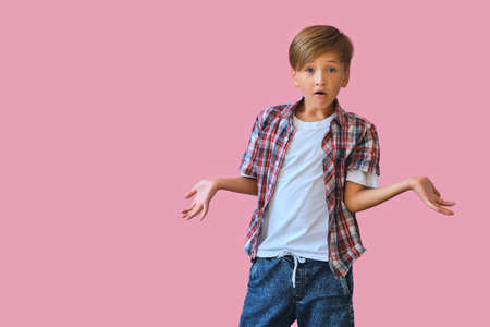 Young surprised teen boy with raised hands to the side isolated on pink background.