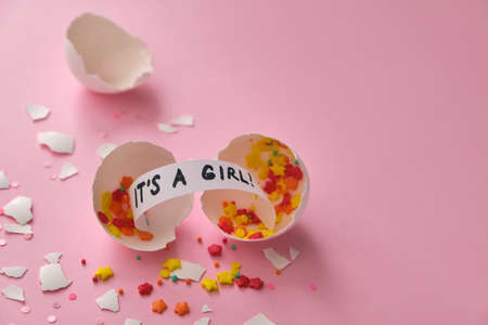 gender party. boy or girl. Broken egg shell with colored confetti and message It's a girl, on pink background. Celebration concept when the gender of the child becomes knownの写真素材