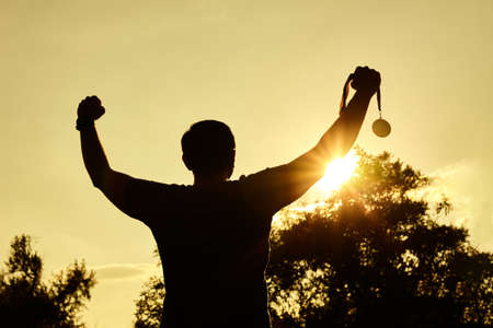Silhouette man victory raising hands and holding gold medal with sunset sky. Motivation and success concept.の写真素材