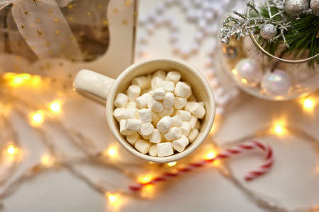 Cup of Chocolate with Marshmallows, Christmas Decorations on white table, candy cane and gift boxの写真素材