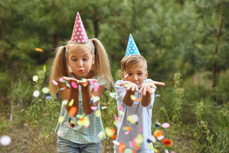 Little Girl and boy having fun celebrating Birthday while blowing confetti at party outdoor - Selective Focusの写真素材