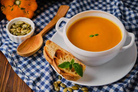 Homemade pumpkin soup with cream, croutons, pumpkin seeds and basil on rustic wooden background, selective focusの写真素材