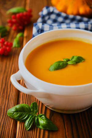 Homemade pumpkin soup with cream, croutons, pumpkin seeds and basil on rustic wooden background, selective focusの写真素材