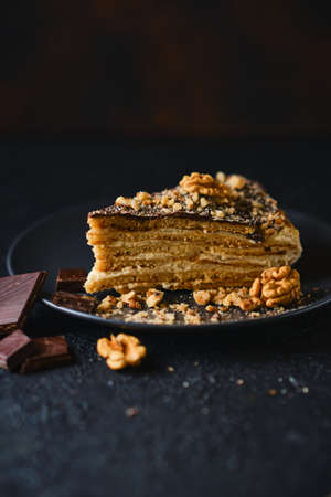 Biscuit cake with sour cream, nuts and chocolate glaze, on a black plate with chocolate on a dark textured background, Selective focusの写真素材