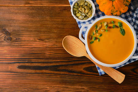 Homemade pumpkin soup with cream, pumpkin seeds and basil on rustic wooden background, selective focus, copy spaceの写真素材