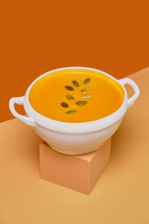 Pumpkin soup decorated pumpkin seeds isolated on orange background. Monochrome, minimalism. View from above. Copy space.の写真素材