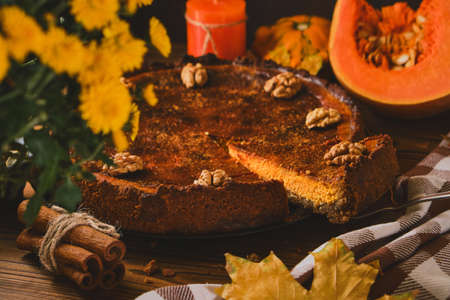 Traditional Pumpkin pie with walnuts and ingredients for cooking on a wooden table. Autumn food in dark styleの写真素材