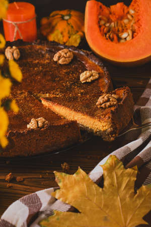 Fresh homemade pumpkin cheesecake with whipped cream and walnuts, with ingredients and autumn flowers on the wooden tableの写真素材