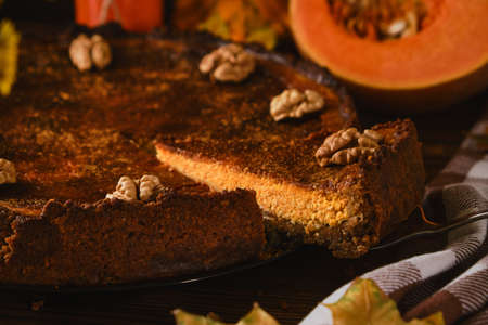Fresh homemade pumpkin cheesecake with whipped cream and walnuts, with ingredients and autumn flowers on the wooden tableの写真素材