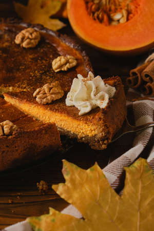 Fresh homemade pumpkin cheesecake with whipped cream and walnuts, with ingredients and autumn flowers on the wooden tableの写真素材