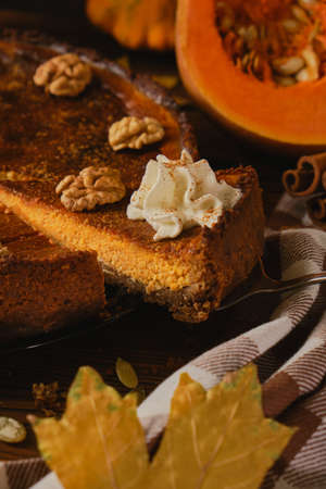 Fresh homemade pumpkin cheesecake with whipped cream and walnuts, with ingredients and autumn flowers on the wooden tableの写真素材