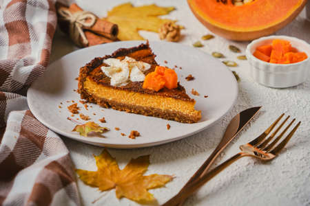 Homemade pumpkin cheesecake decorated with whipped cream on gray plate. selective focus, white textured backgroundの写真素材