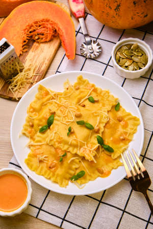 Homemade Pumpkin Ravioli with ricotta cheese served basil, pine nuts and hard cheese on white plate surrounded by ingredients on wooden table. Selective focus.の写真素材