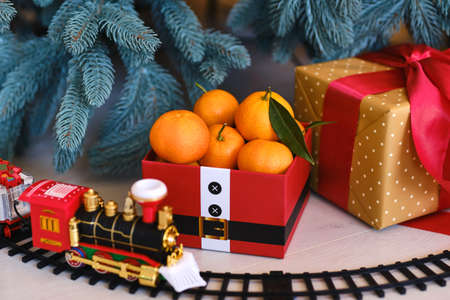Red gift box of fresh mandarin fruits in a Festive composition on the background of a Christmas treeの写真素材
