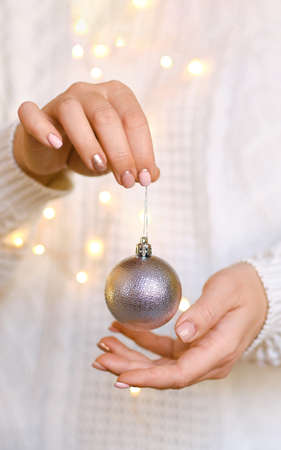 Woman in white warm woolen sweater holding toy decorative ball in hands, copy space. Christmas, new year holiday celebration concept. Selective focusの写真素材