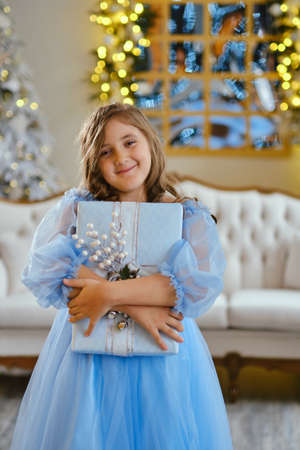 cute little girl in light blue dress with gift box against Christmas tree. Xmas holiday conceptの写真素材