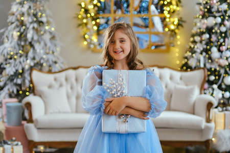 cute little girl in light blue dress with gift box against Christmas tree. Xmas holiday conceptの写真素材