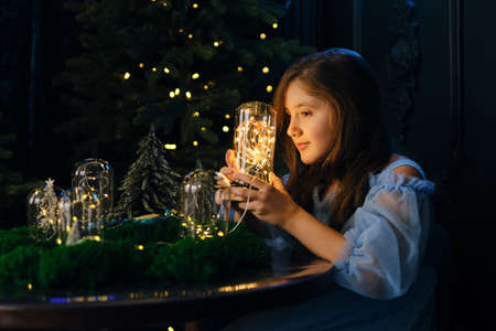 A little girl holds a glass flask with magic lights, in a dark interior.の写真素材