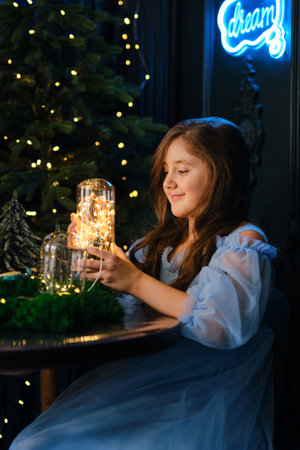 A little girl holds a glass flask with magic lights, in a dark interior.の写真素材