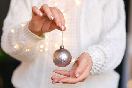 Woman in white warm woolen sweater holding toy decorative ball in hands, copy space. Christmas, new year holiday celebration concept. Selective focus, Cozy Vibesの写真素材