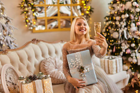 Beautiful elegant young blonde women in fashionable dress with glass of champagne celebrating Christmas and New Year's Eve in a decorated roomの写真素材