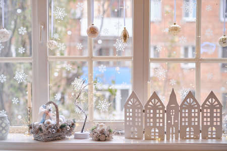 winter decor on windowsill with decor, basket with Christmas balls, wooden houses, candles and lightsの写真素材