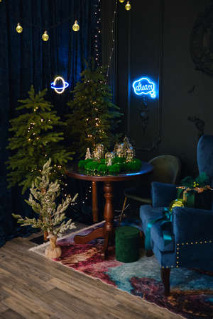 Blue and green Christmas interior. A fairy interior with a green wall, blue armchair, round table on which there are glowing bulbs decorated with moss and Christmas trees with lights and neon signsの写真素材