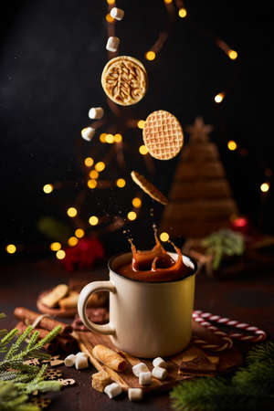 waffle cookies over a mug of Christmas hot chocolate or cacao. Winter drink on a dark background with Christmas decorations. Action food photo, levitation food, sweet dessertの写真素材