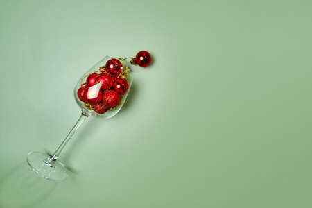 Wine glass filled with red christmas balls on green background. Holiday menu conceptの写真素材