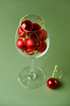 Wine glass filled with red christmas balls on green background. Holiday menu conceptの写真素材