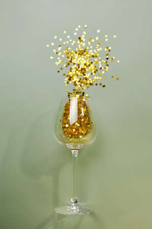 New Year and Christmas party concept. Top view flat lay wine glass with scattered golden star glitter. Copy space. Background minimal style.の写真素材