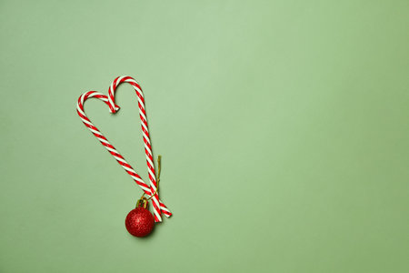 Christmas Card Background. Christmas tree or heart made of candy and New Year decoration. Minimal holiday concept. Candy Canes and red toy balls on green background. Flat lay, top view, copy space.の写真素材