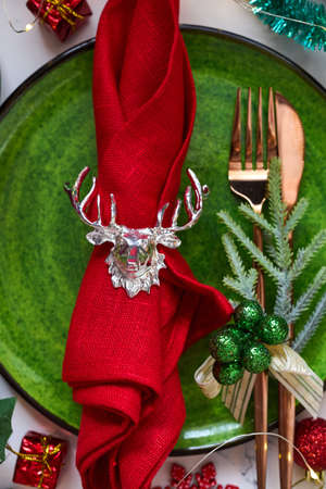 Traditional Christmas table place setting close up. Golden cutlery, linen napkin with deer ring, spruce branches. Holidays background. Flat lay, top view, selective focus.の写真素材
