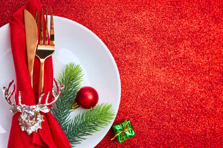 Christmas And New Year Holiday Table Setting with copy space, green plate, red background. Celebration. Place setting for Christmas Dinner. Red holiday decorationsの写真素材