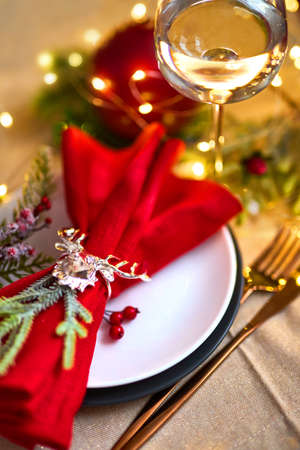 Traditional Christmas table place setting close up. Golden cutlery, linen napkin with deer ring, spruce branches and glass of wine. Holidays background. Selective focus, garland, bokeh.の写真素材