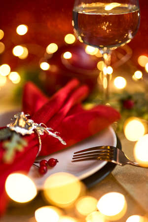 Traditional Christmas table place setting close up. Golden cutlery, linen napkin with deer ring, spruce branches and glass of wine. Holidays background. Selective focus, garland, bokeh.の写真素材