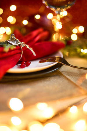Traditional Christmas table place setting close up. Golden cutlery, linen napkin with deer ring, spruce branches. Holidays background. Selective focus, garland, bokeh.の写真素材