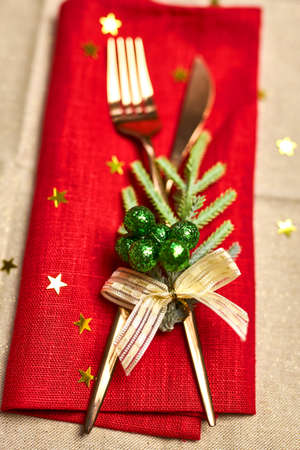 Traditional Christmas table place setting close up. Golden cutlery, linen napkin with deer ring, spruce branches. Holidays background. Selective focus, garland, bokeh.の写真素材