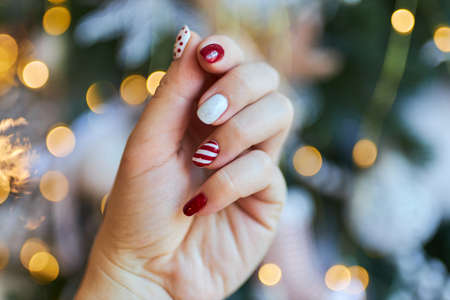 Christmas New Year manicure abstract nail design. Beautiful manicured woman's hand against the background of the christmas treeの写真素材
