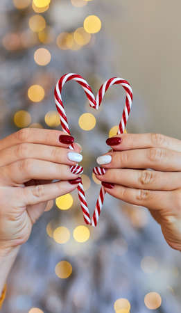 Christmas New Year manicure abstract nail design. Beautiful manicured woman's hand holding candy canes ornaments in the shape of a heartの写真素材