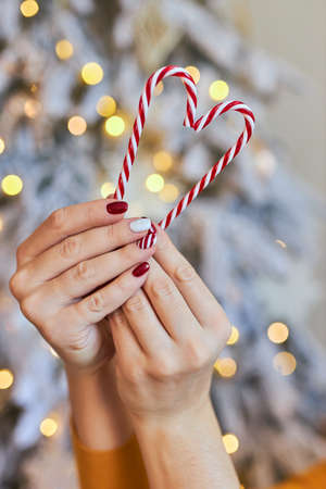 Christmas New Year manicure abstract nail design. Beautiful manicured woman's hand holding candy canes ornaments in the shape of a heartの写真素材