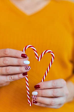 Christmas New Year manicure abstract nail design. Beautiful manicured woman's hand holding candy canes ornaments in the shape of a heartの写真素材
