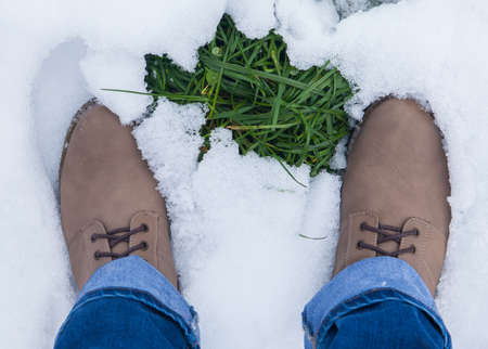 Top view woman legs in hiking leather boots on covered snow forest glade and green grass, concept activity and adventure outdoorsの写真素材