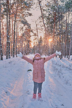 Child playing with snow in winter. Little girl in pink jacket and knitted hat catching snowflakes in winter park on Christmas. Kid play and jump in snowy forest. Snow ball fight for children.の写真素材